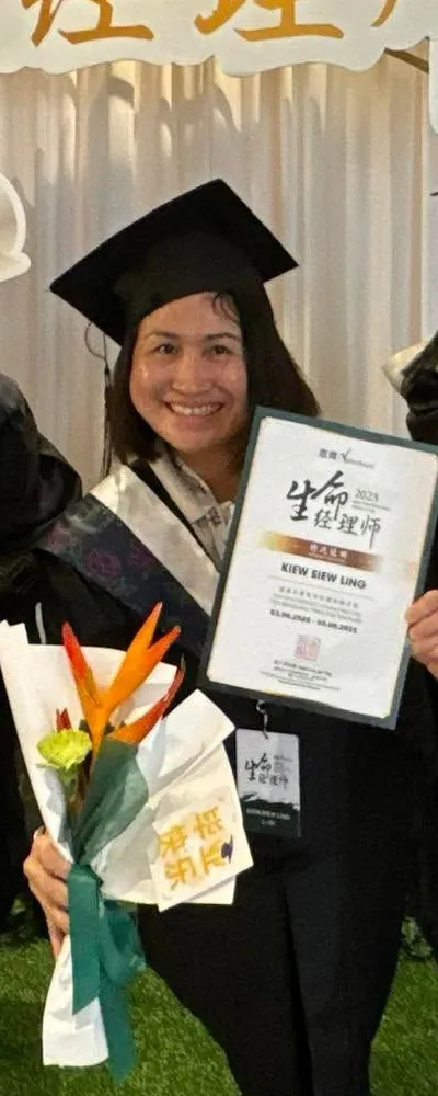 秀玲穿毕业袍，手拿写着 KIEW SIEW LING 的生命经理师结业证书