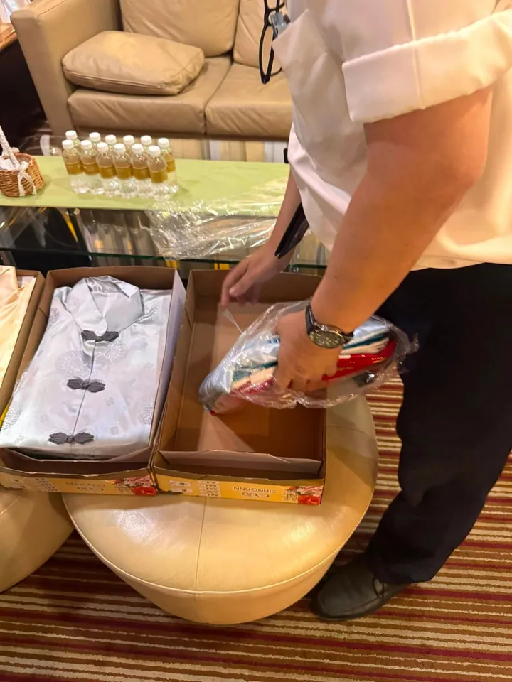 一只手从纸盒里取出一套叠好的银白缎面寿衣