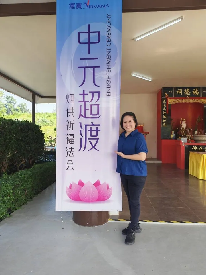 秀玲站在中元超渡烟供祈福法会的直立海报旁
